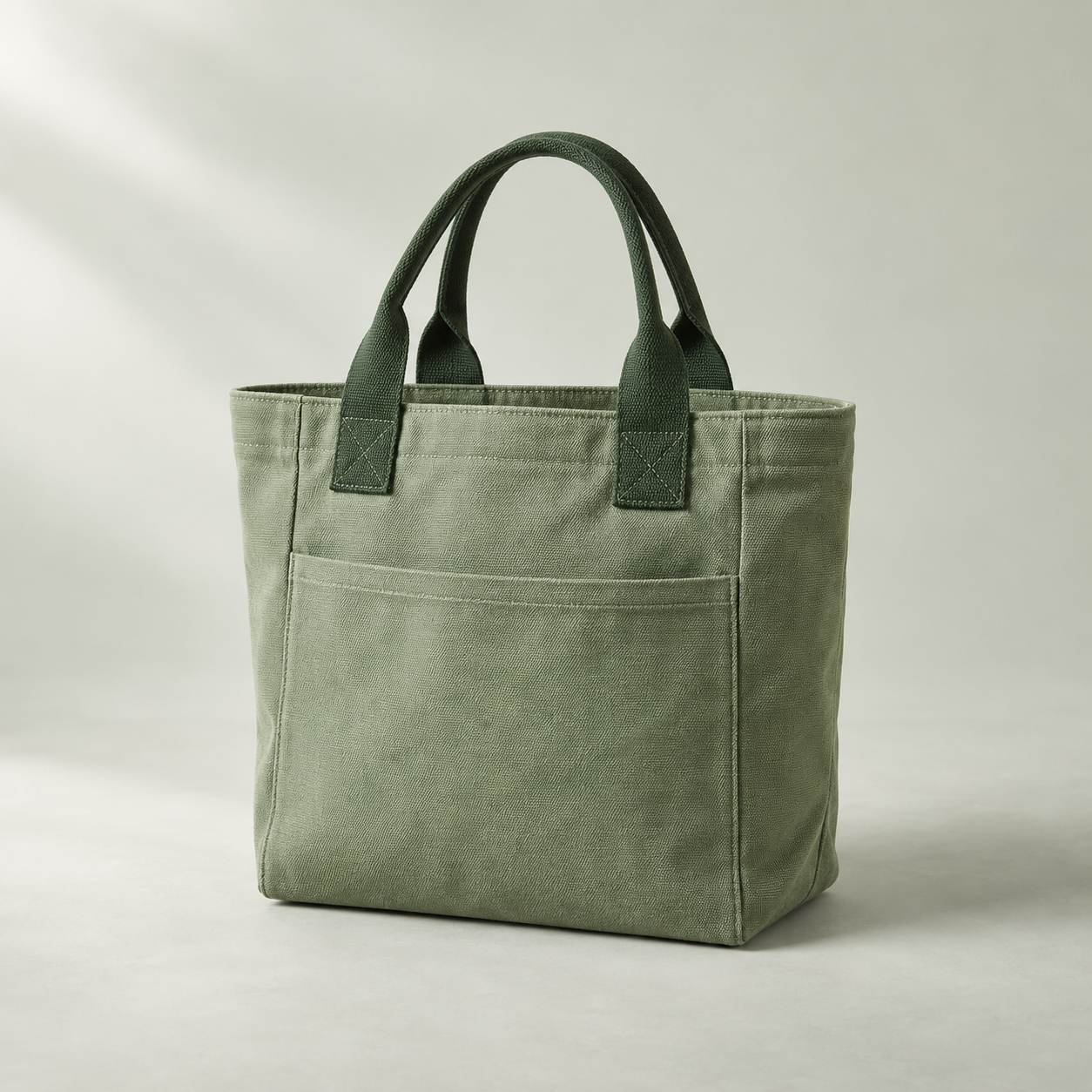 Illustrative sage green tote bag with dark green handles and an exterior front pocket.